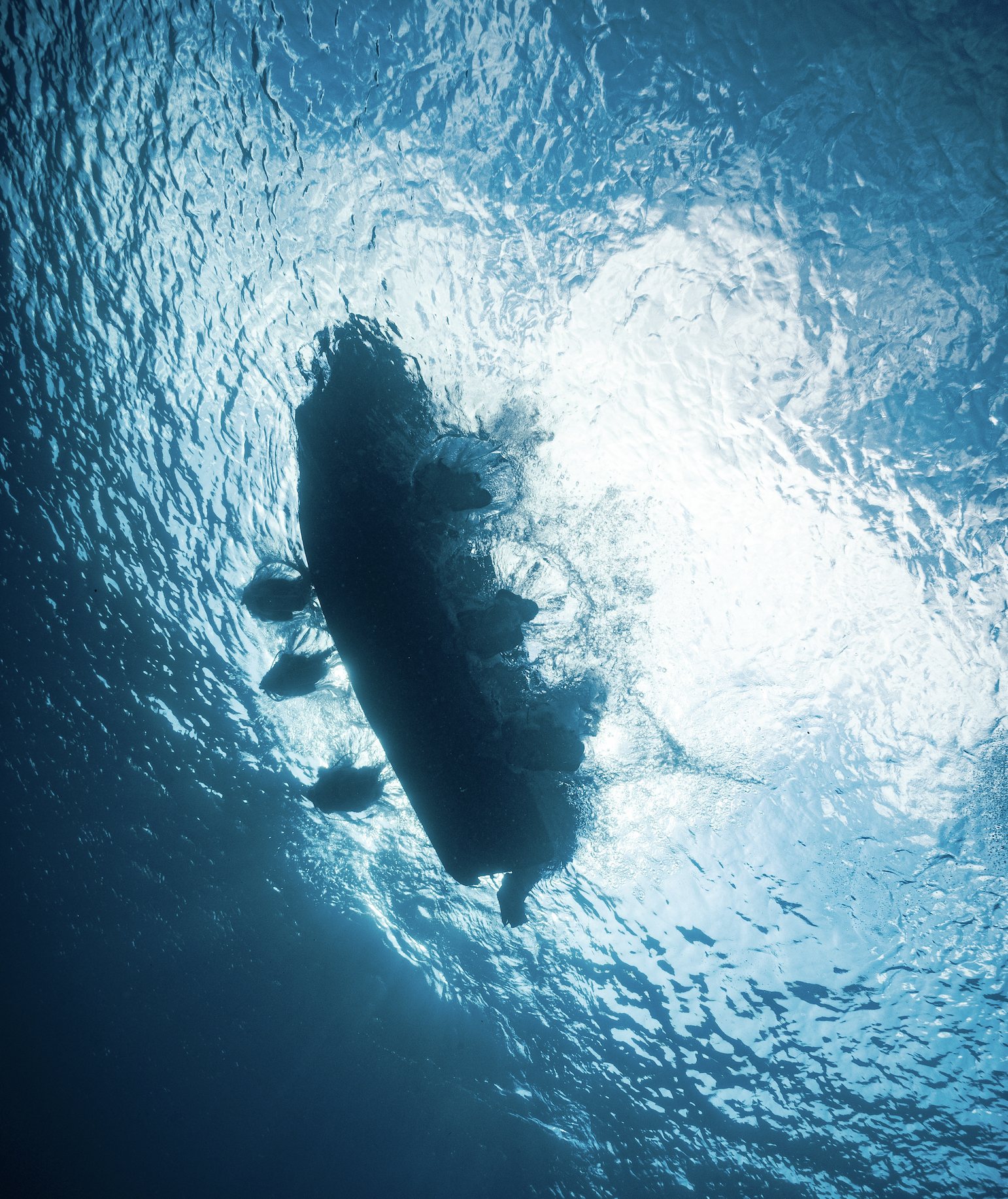 Looking up from underwater at the hull of a dive boat silhouetted against sunlit water.