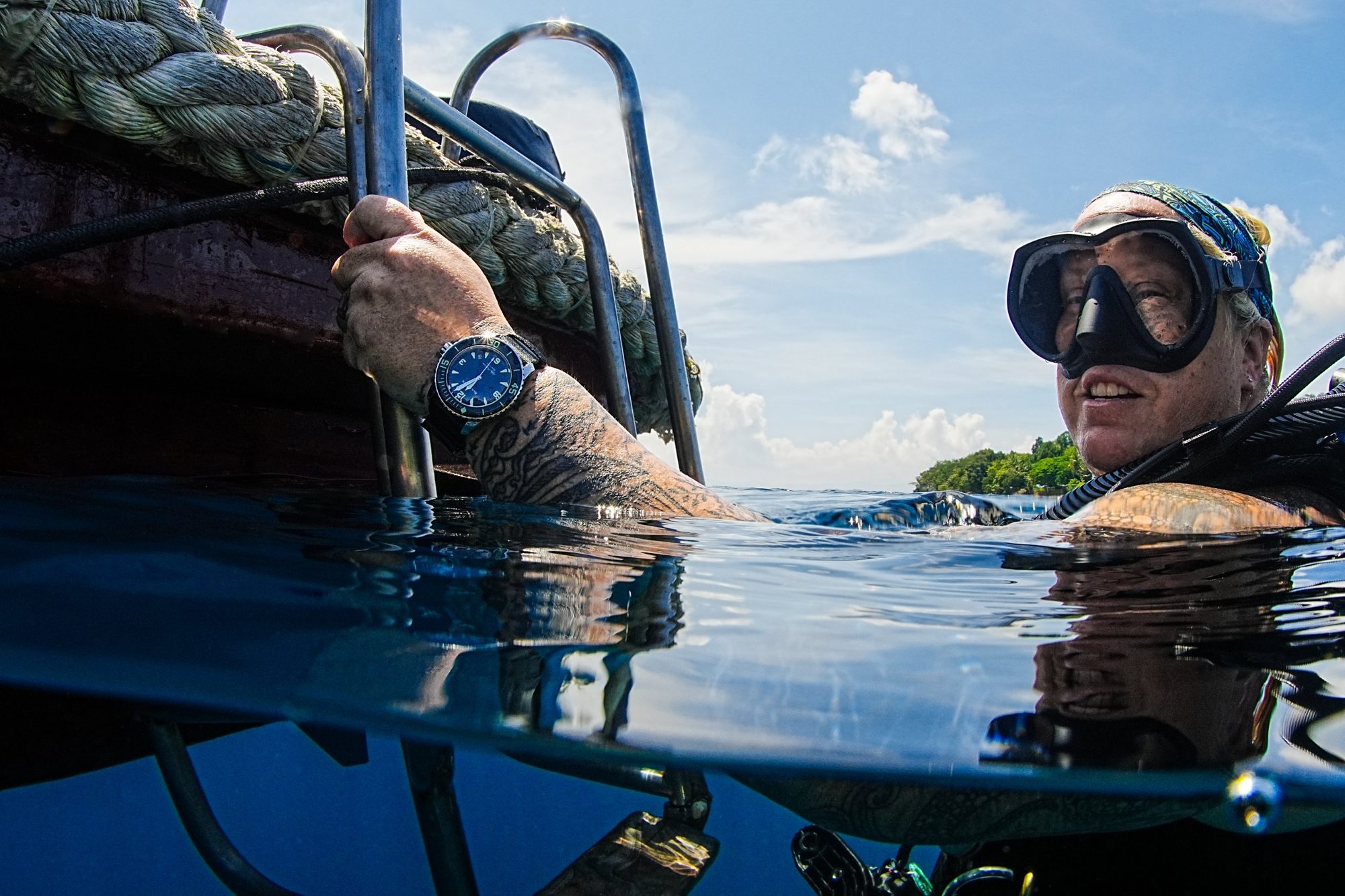 Me at the surface beside a boat ladder, smiling in my mask, after a dive.